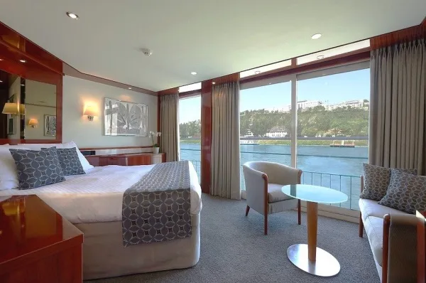 Beispielbild 2-Bett Oberdeck deluxe Suite mit Panorama-Fenstern und französischem Balkon sowie großem Doppelbett und einem Tisch.