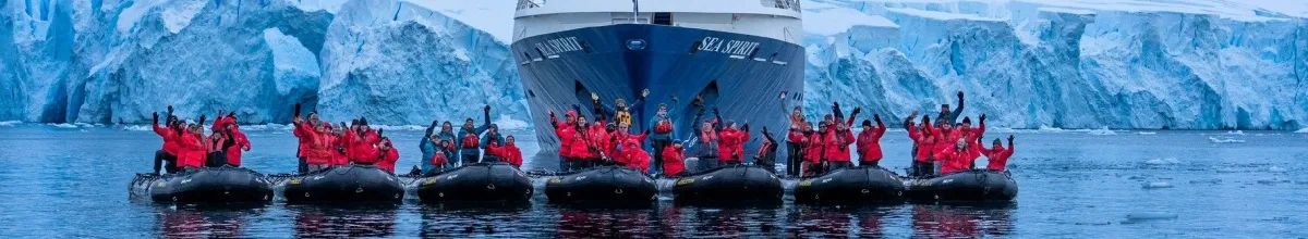 Die MS Sea Spirit vor riesigen antarktischen Gletschern. Vor den Eisbergen schwimmt das Expeditionsschiff MS Sea Spirit. Vor dem Schiff liegen 7 Zodiacs mit Passagieren.