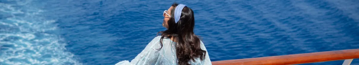 Eine Frau an der Reling eines Schiffes von Celestyal Cruises schaut auf das offene Meer.