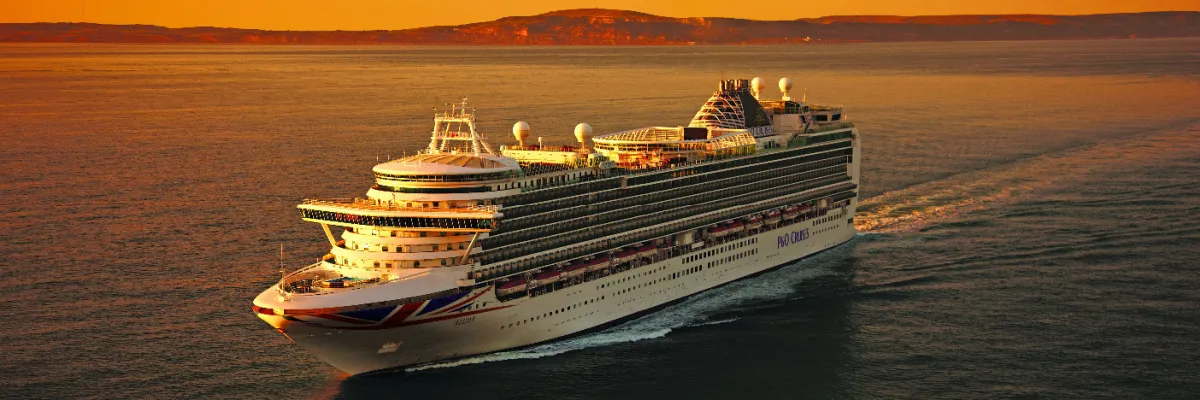 Das Kreuzfahrtschiff Azura von P&O Cruises vor einer Küste bei Sonennuntergang.