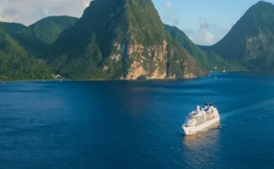 Eines der Luxuskreuzfahrtschiffe von Seabourn in der Karibik vor riesigen Bergen, die aus dem Meer ragen.