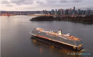 Die MS Koningsdam vor einer Großstadt auf dem Wasser hell beleuchtet.