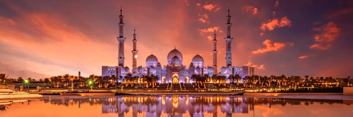 Die Scheich-Zayid-Moschee in Abu Dhabi reflektiert bei Sonnenuntergang auf dem Wasser.