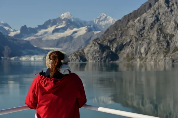 Eine Alleinreisende auf einer Polar-Kreuzfahrt Eine Frau steht am Bug eines Kreuzfahrtschiffes und schaut auf die bergige Landschaft.