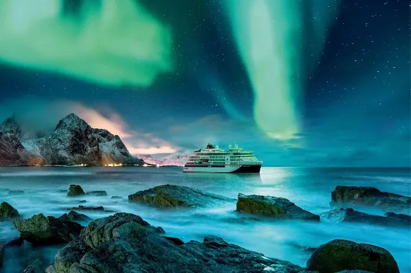 Ein Expeditionsschiff von Hapag-Lloyd in Nordland unter umwerfenden grün-blauen Polarlichtern, umgeben von Felsen.