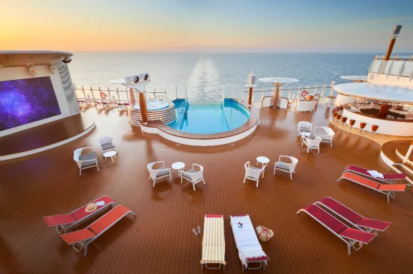 Das Pooldeck der AIDAcosma in warmen Farben, mit zahlreichen Liegen, luxuriöser Ausstattung, dem Pool und dem Blick übers Meer.