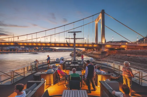 MS Thurgau Prestige Auf dem Sonnendeck der MS Thurgau Prestige sind mehrere Personen am Abendhimmel und unterhalten sich und schauen auf den Fluss.
