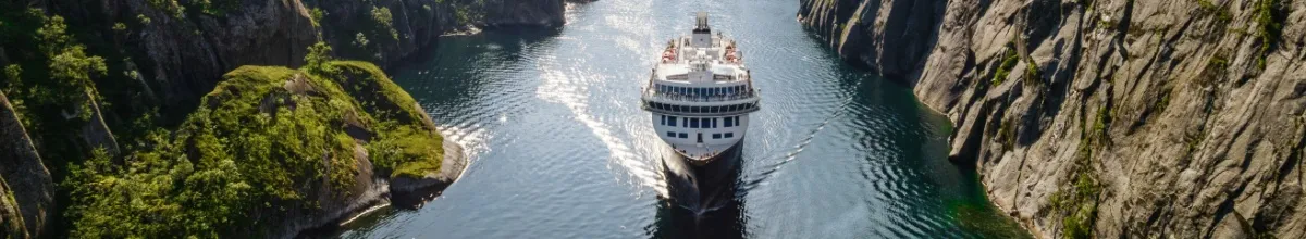 Ein Havila Schiff fährt elegant durch einen glitzernden norwegischen Fjord bei bestem Wetter.