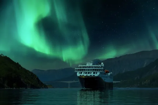 Die Havila Castor in Norwegen. Am Himmer erstrahlen grüne Polarlichter. Havila Voyages verspricht Ihnen Nordlichter bei jeder 12-Tage Route.