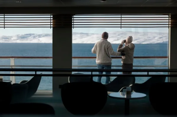 Ein Paar schaut mit dem Fernglas aus den Panoramafenstern der Havila Voyages Flotte.