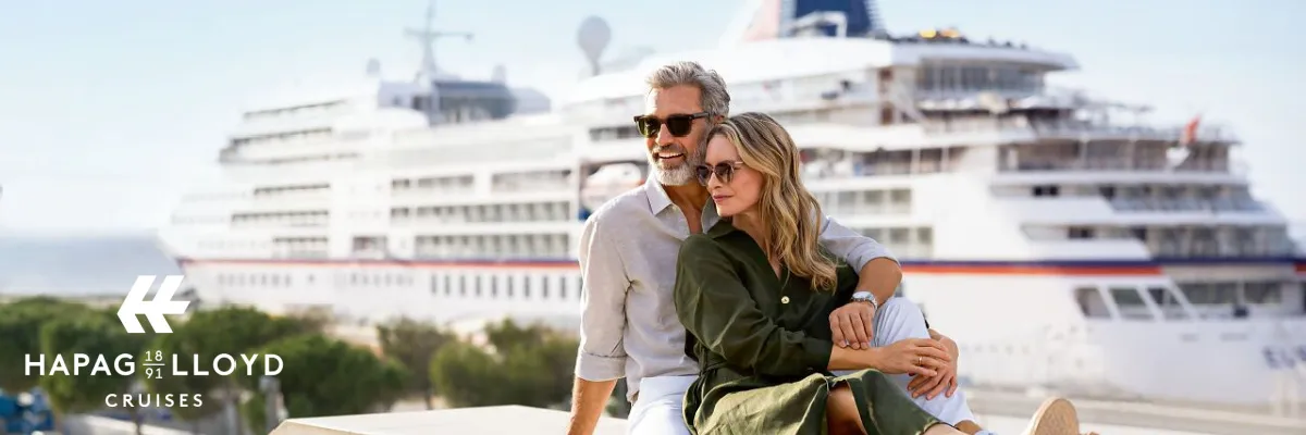in elegantes Paar entspannt an Land vor dem im Hafen liegenden Luxuskreuzfahrtschiff MS Europa von Hapag-Lloyd Cruises.