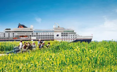 Hapag-Lloyd Cruises - Tipp der Woche: Diesmal mit Kreuzfahrten in den europäischen Norden und nach Alaska. Ein Schiff der HANSEATIC Expeditionsklasse vor einem grünen Flussdelta auf dem ein Zodiac mit Gästen fährt.