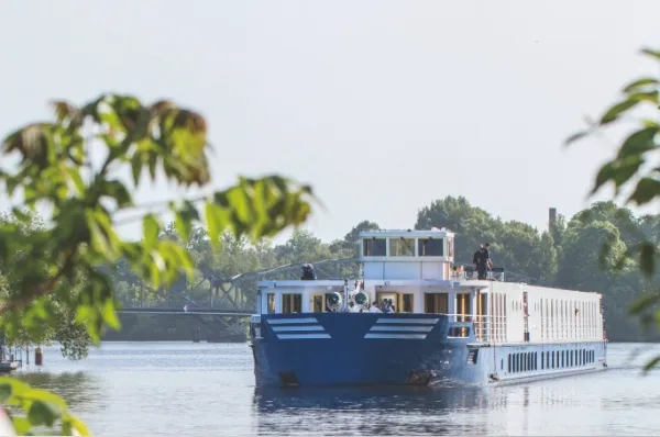 Die MS Thurgau Chopin auf dem Fluss, im Vordergrund ragen grüne Äste in das Bild.