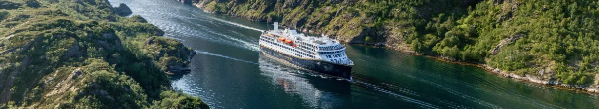 Norwegen mit der Havila Voyages Flotte Eines der Havila Voyages Schiffe im Trollfjord in Norwegen umgeben von grünen Bergen.