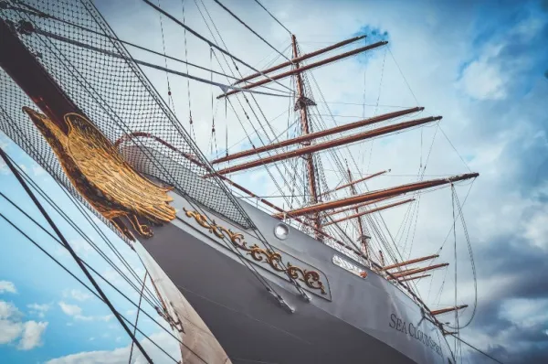 Die vordere Spitze der Sea Cloud Spirit mit einem goldenen Adler verziert, sowie die Segel des Schiffes unter blauem Himmel.