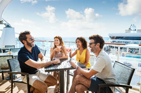 Gäste sitzen in einer offenen Bar auf einem Schiff von NCL Eine Gruppe von Gästen sitzt und lacht auf einer Deckbar der NCL Flotte.