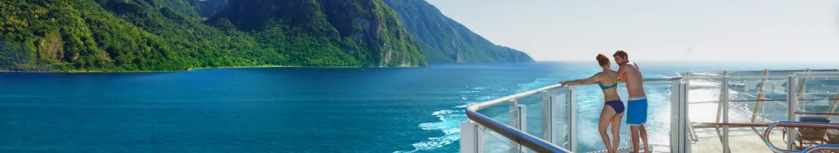 Ein Pärchen genießt ihren Urlaub dank NCL Flash Sale Ein Pärchen an der Reling eines Schiffes von NCL vor der Küste von St. Lucia in der Karibik.