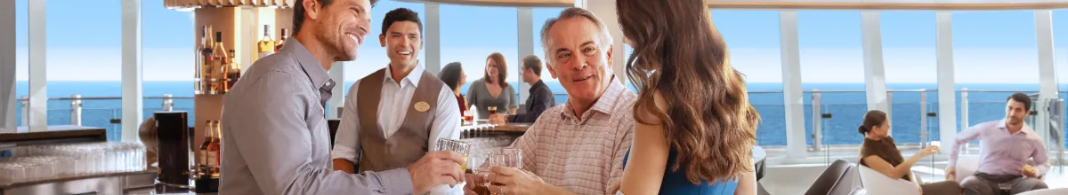 NCL Free at Sea Getränkepaket Upgrade Eine Gruppe stößt an in einem Bordrestaurant, dank des reduzierten Free at Sea Upgrades. Im Hintergrund sind weitere Gäste und die Aussicht über den Ozean.