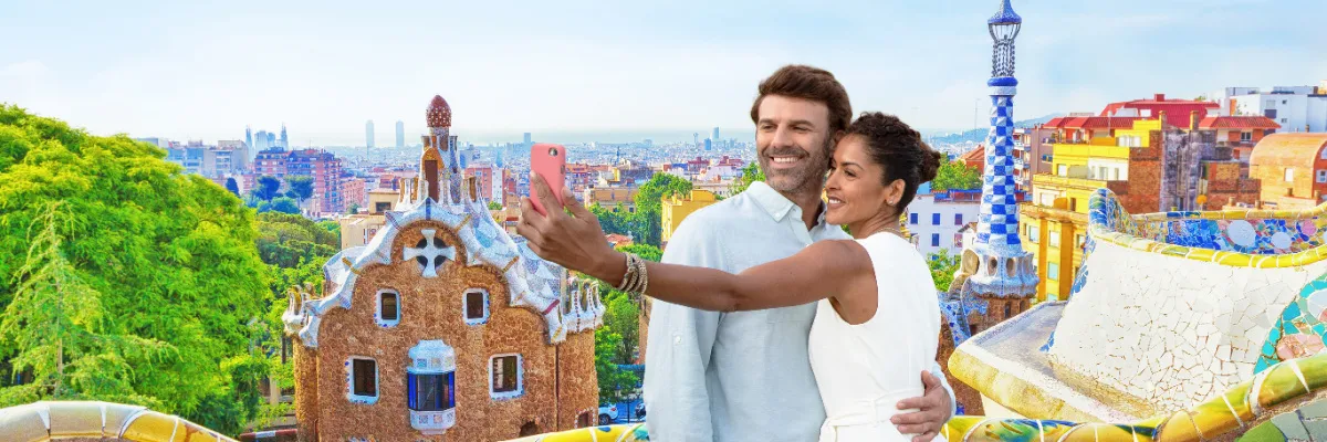 Ein lächelndes Paar macht ein Selfie im farbenfrohen Park Güell in Barcelona während eines Landausflugs einer NCL Europa-Kreuzfahrt.