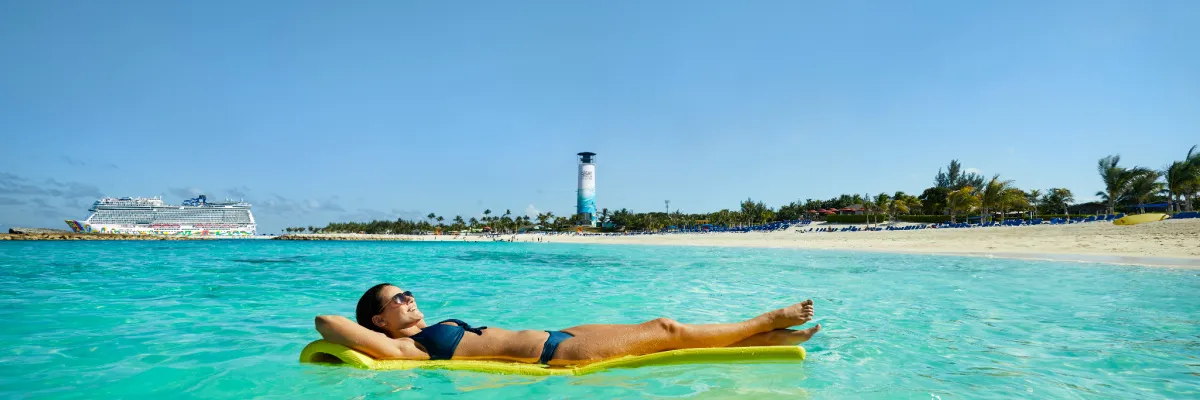 Entspannung auf NCL Privatinsel Great Stirrup Cay Eine Frau entspannt auf einer Luftmatratze im türkisen Wasser vor der NCL Privatinsel Great Stirrup Cay, im Hintergrund liegt ein NCL Kreuzfahrtschiff vor Anker.
