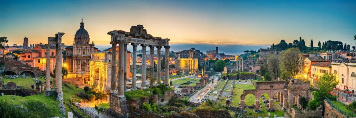Panorama-Ansicht des beleuchteten Forum Romanum in Rom mit den Ruinen des Saturn-Tempels während der Abenddämmerung.
