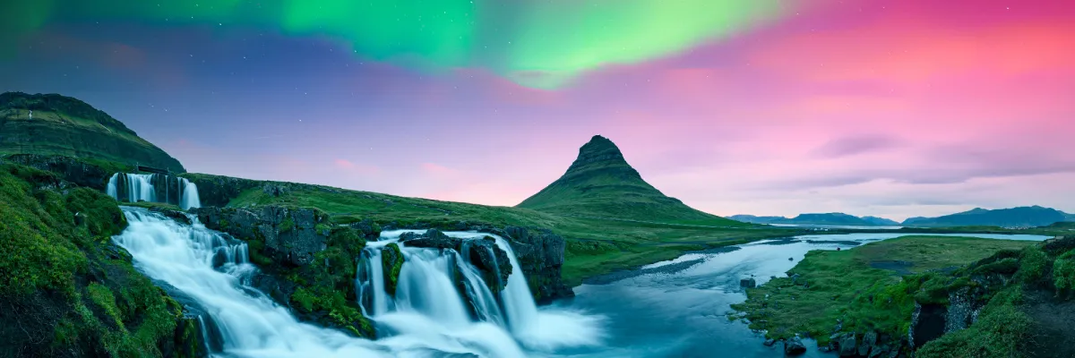 Die Kirkjufellsfoss Wasserfälle und der Berg Kirkjufell in Island unter farbenprächtigen Nordlichtern während einer NCL Nordeuropa Kreuzfahrt.