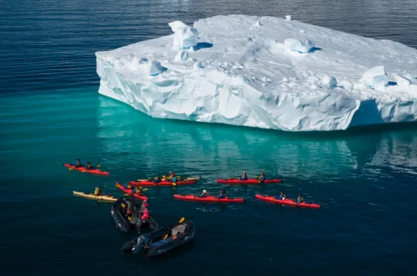 Eine Gruppe fährt Kajak vor einem Gletscher. Zwei Zodiacs von Poseidon Expeditions haben sie auf das offene Meer gebracht.