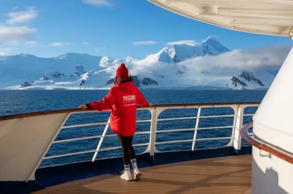 Eine Frau in einer roten Expeditionsjacke von Poseidon Expeditions steht an der Reling der MS Sea Spirit und schaut auf die Eislandschaft und das Meer.