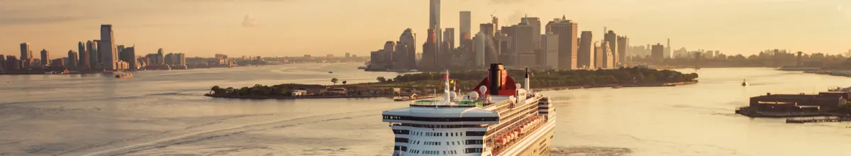 Die Queen Mary 2, wie sie in der Abendsonne den Hafen von New York verlässt. Im Hintergrund die Skyline von Manhattan.