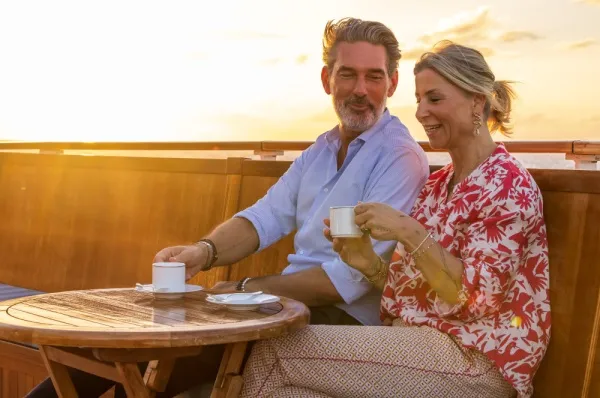 Ein Mann und eine Frau sitzen an einem Tisch und trinken ein Heißgetränk bei Sonnenuntergang.