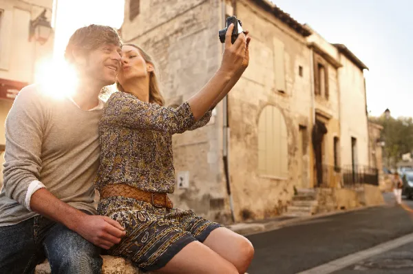 Ein glückliches Paar macht ein Selfie während eines Stadtbummels in einer historischen europäischen Altstadt im warmen Licht der Abendsonne.