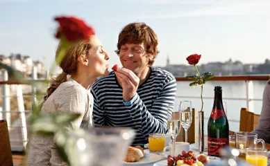 Ein Paar genießt ein romantisches Frühstück mit Champagner und Erdbeeren auf dem Sonnendeck einer A-ROSA Flusskreuzfahrt zum Valentins-Special 2026.