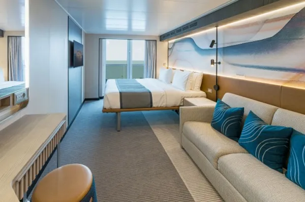 Eine Balkonkabine mit Doppelbett und blauen Akzenten auf der Norwegian Aura.