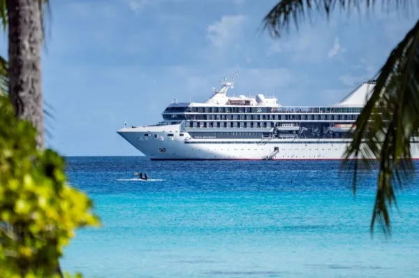 Die Le Paul Gauguin im Pazifischen Ozean an der Küste von Französisch-Polynesien eingerahmt durch Palmen.