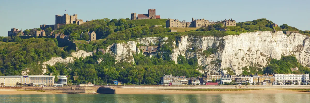 Panoramablick auf die berühmten weißen Kreidefelsen von Dover und das historische Dover Castle auf dem Hügel unter blauem Himmel.