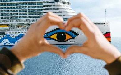 Hände formen ein Herz vor dem ikonischen Auge eines AIDA Schiffes auf dem Meer zum 30. Jubiläum der Reederei.