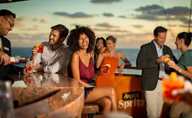 Italienische Lebensfreude und Sonnenuntergang an Bord von Costa Eine Gruppe von Reisenden genießt Aperol Spritz an einer Bar auf dem Deck eines Costa Kreuzfahrtschiffes während eines malerischen Sonnenuntergangs.