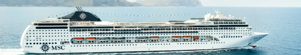 Seitenansicht des Kreuzfahrtschiffs MSC Lirica, das auf dem Meer fährt. Man sieht die weißen Aufbauten, Reihen von Rettungsbooten, das MSC-Logo am Bug und den markanten Schornstein. Im Hintergrund sind Berge an einer Küste zu erkennen.
