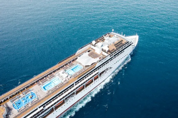 Luftaufnahme der MSC Lirica, die auf dem blauen Meer fährt. Deutlich zu sehen ist das obere Deck mit zwei Swimmingpools, einem bunten Aqua Park für Kinder und zahlreichen Sonnenliegen