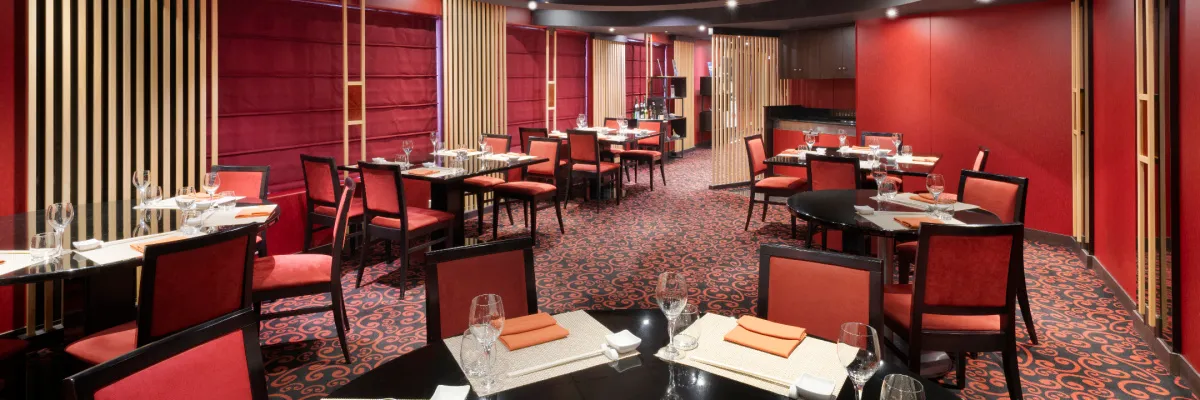 Innenansicht der Kaito Sushi Bar auf der MSC Lirica. Das Restaurant ist in eleganten Rot- und Schwarztönen gehalten, mit dunklen Tischen, rot gepolsterten Stühlen und modernen Holzelementen als Raumtrenner.