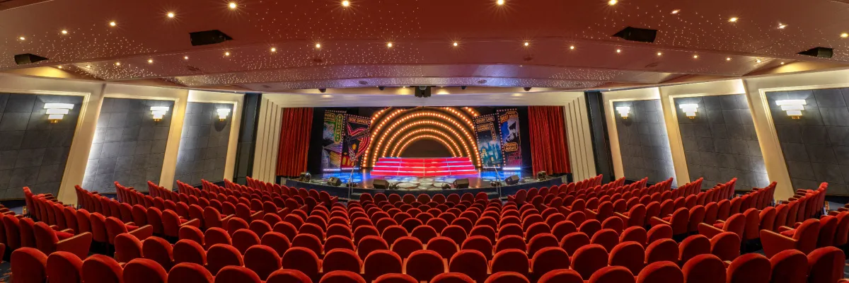 Innenansicht des eleganten Broadway Theaters an Bord der MSC Lirica. Der Raum ist mit Reihen von roten Samtsitzen ausgestattet, die sich vor einer großen Bühne befinden.