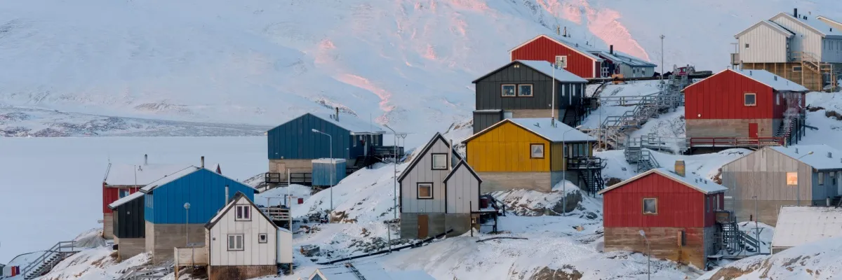 Bunte Häuser auf einem verschneiten Berg in Grönland mit Eisflächen im Hintergrund.
