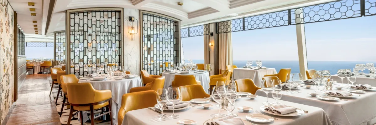 Ein Restaurant der Oceania Cruises mit ockerfarbener Bestuhlung und Panoramafenstern.