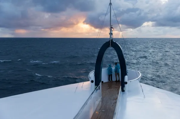 Der Aussichtspunkt "Swans Nest" auf der SH Vega. Zwei Personen mit Swan Hellenic Parkas stehen dort und schauen auf den Sonnenuntergang.