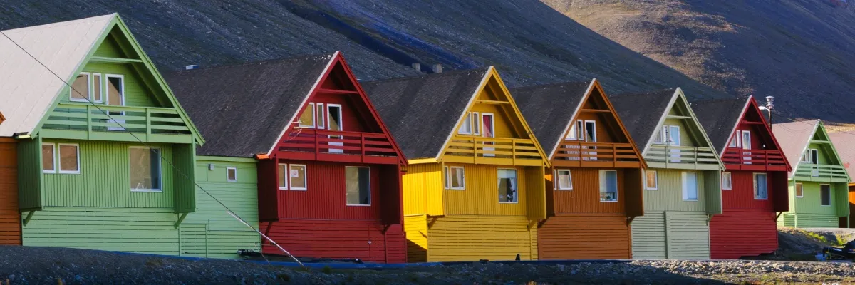 Mit Swan Hellenic in die Arktis Bunte Häuser in einer Reihe auf Longyearbyen im Sommer bei Sonnenschein. Im Hintergrund türmt sich ein Berg auf.