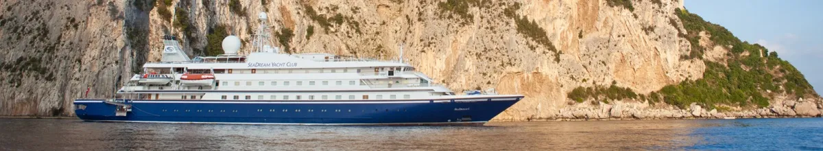 SeaDream Yacht Club: Die Reederei Die SeaDream I legt gerade ab und fährt an einem felsigen Hintergrund Richtung offenes Meer, um ihre Reise zu starten.