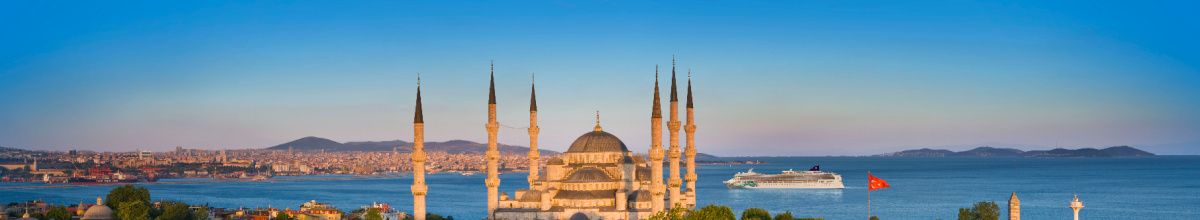 Panorama-Aufnahme der Blauen Moschee in Istanbul bei Sonnenuntergang, während ein Schiff von Norwegian Cruise Line majestätisch durch den Bosporus gleitet.
