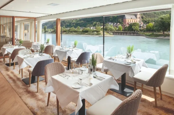 Blick auf Tische und Stühle im Restaurant der MS Thurgau Gold, im Hintergrund Blick auf eine Burg am Fluss.