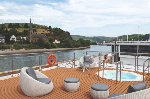 Sonnendeck an Bord der MS Thurgau Gold mit bequemen Sitzmöbeln, im Hintergrund Flusslandschaften.