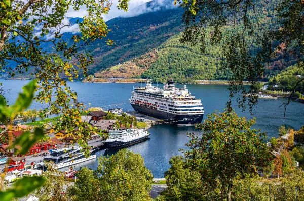 Das Kreuzfahrtschiff VASCO DA GAMA von nicko cruises im Hafen eines norwegischen Fjords, eingerahmt von herbstlichen Zweigen mit roten Beeren vor einer majestätischen Bergkulisse.